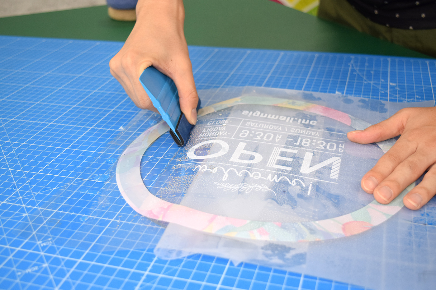 透明アクリルに貼ったwelcome OPENデザインを、スキージーで気泡を押し出しながら圧着している様子