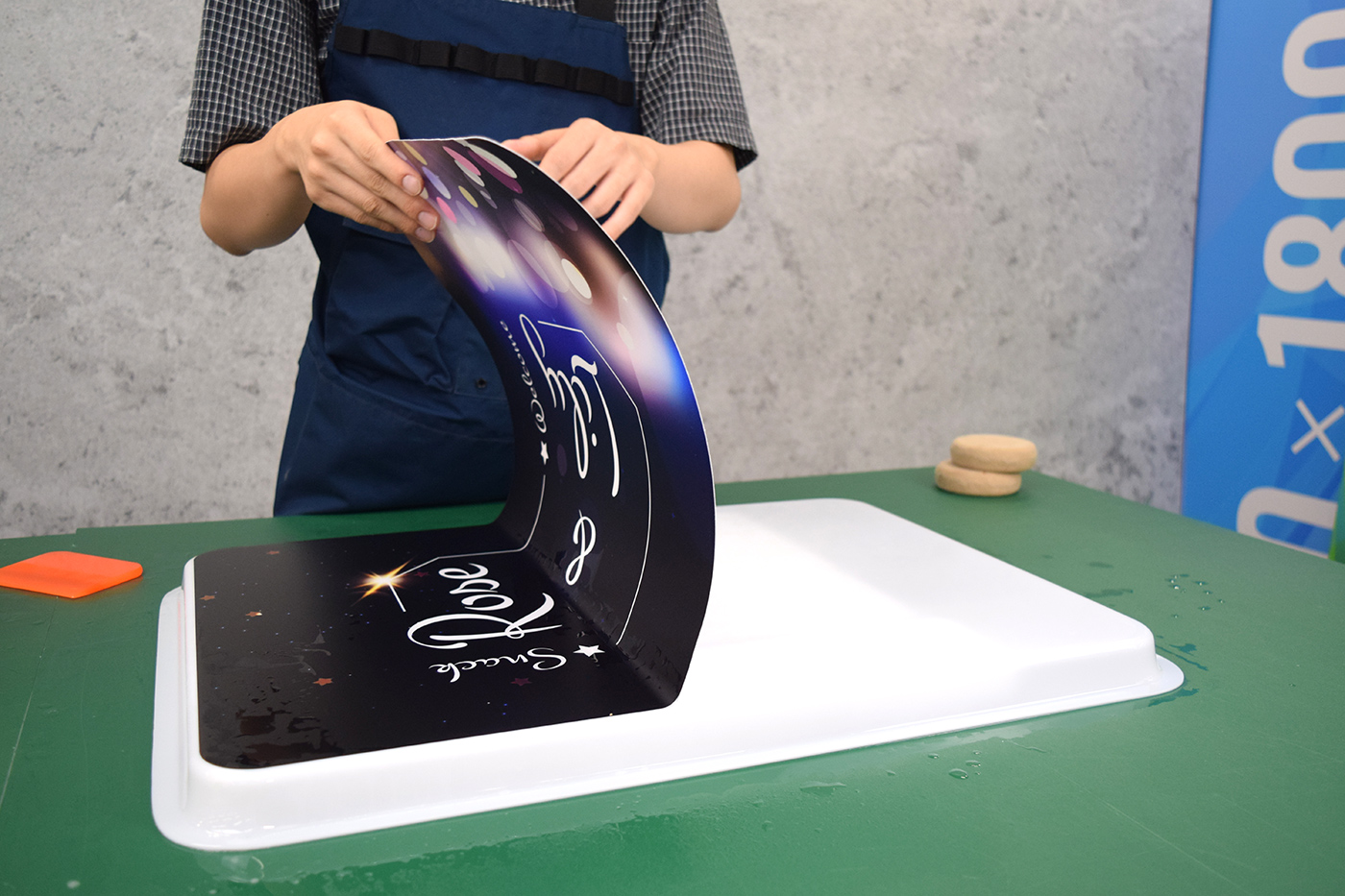 シートを大きくめくり上げて糊面に施工液を吹き付ける様子