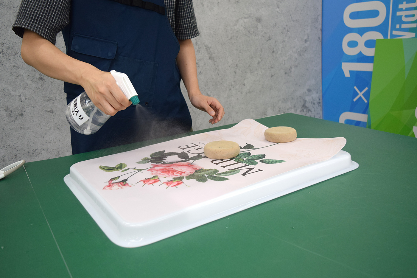 霧吹きで表示面板とシートの糊面に施工液を吹き付ける様子