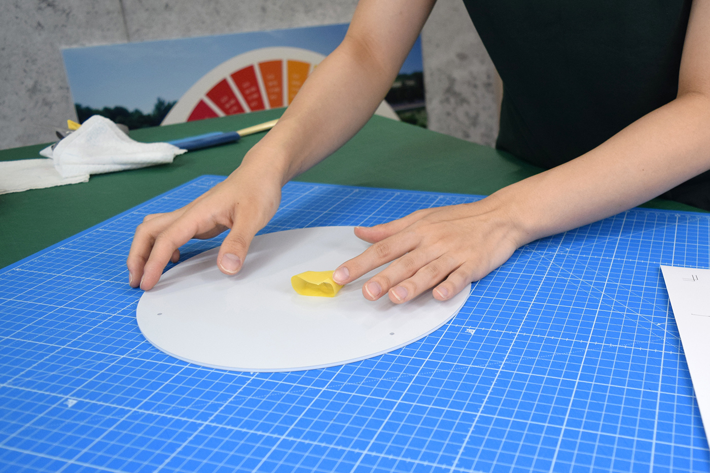 円形のアルミ複合板の面板に、位置合わせ用のマスキングテープを貼っている様子