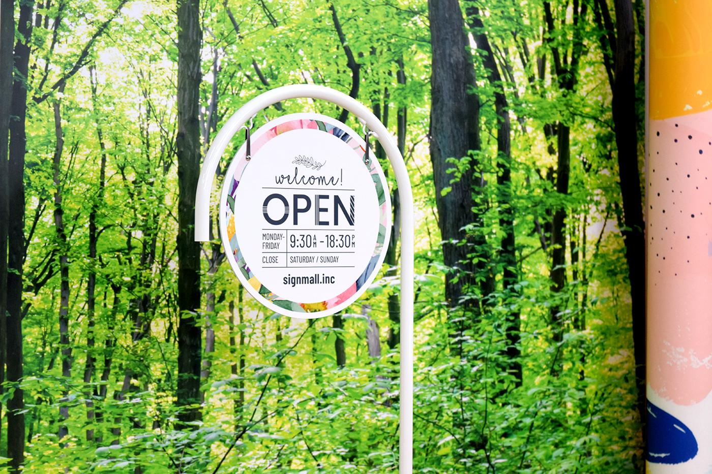 森の背景の前に立つ、白いP型サインスタンド。円形面板の白地welcome OPENデザイン面